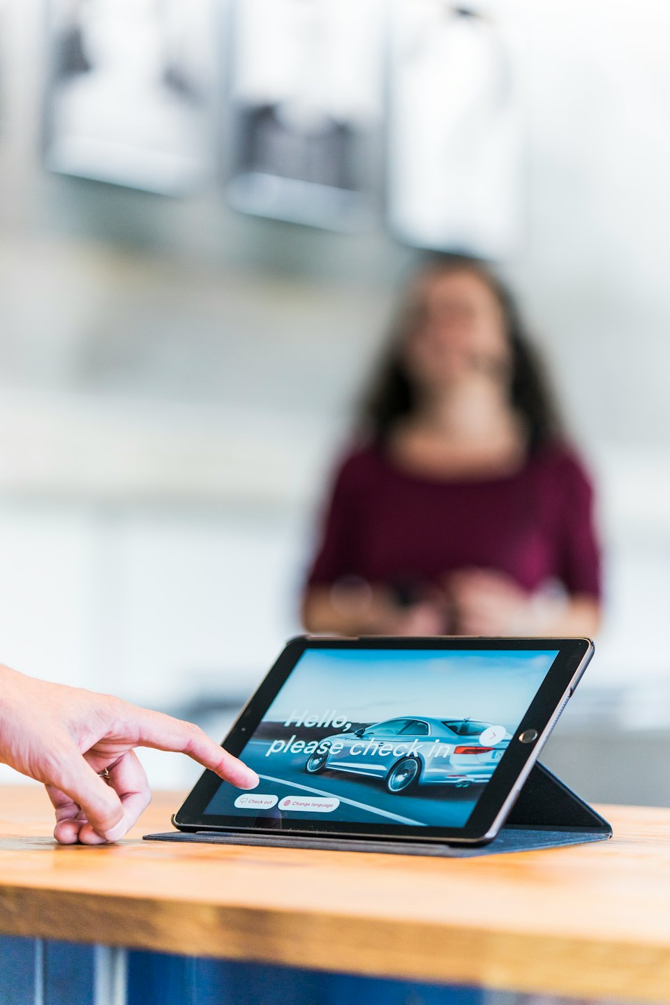 Hand taps tablet showing digital check-in for a car.